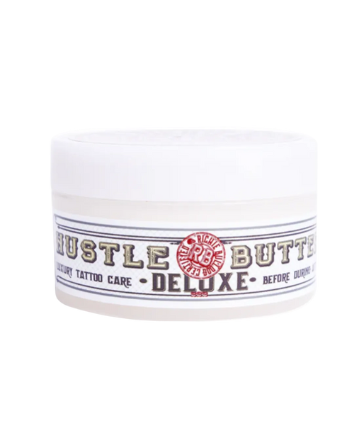 A container of Hustle Butter tattoo care cream, labeled for deluxe size before and after tattoo application.